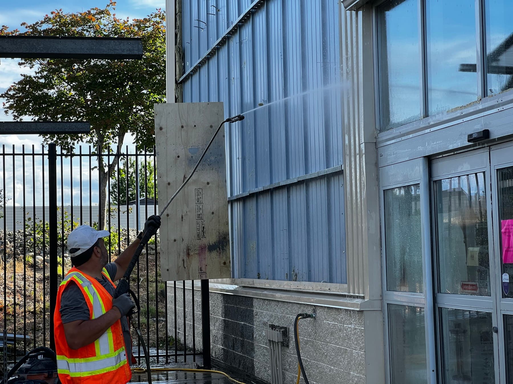 Crew member pressure washing a commercial metal panel wall, half clean and half still dirty
