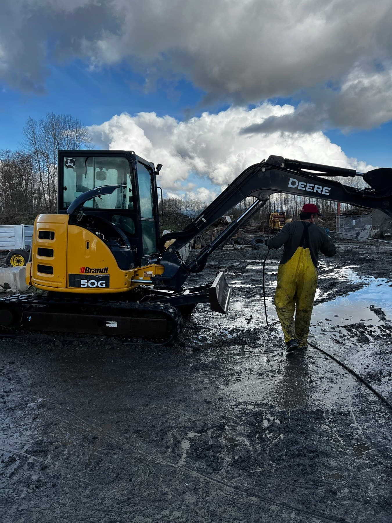 Crew member pressure washing a John Deere excavator on a job site